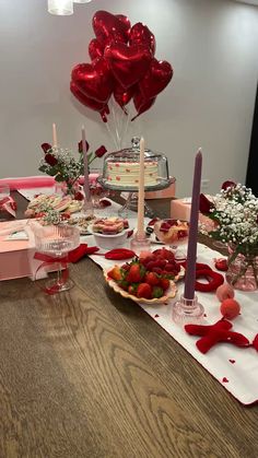 a table topped with lots of red balloons and plates filled with food on top of it