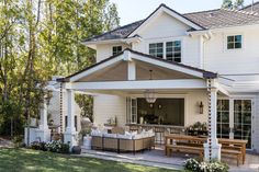 a large white house with lots of windows and furniture on the front porch, along with an outdoor dining area