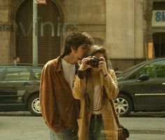 a man and woman standing on the side of a road with a camera in front of them