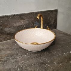 a white bowl sink with gold trim on the edge and a faucet in the middle