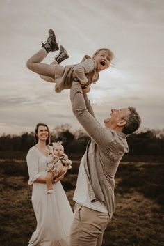 a man holding a baby up in the air while standing next to a woman and child