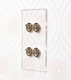 two pairs of gold earrings sitting on top of a glass block in front of a floral wallpaper