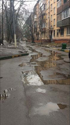 an empty street with puddles on the ground and buildings in the backround