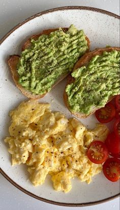 two pieces of toast with avocado and tomatoes on it, sitting on a plate