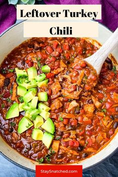 a white bowl filled with chili and avocado next to a wooden spoon in it