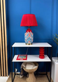 a red lamp sitting on top of a table next to a white shelf with a basket underneath it