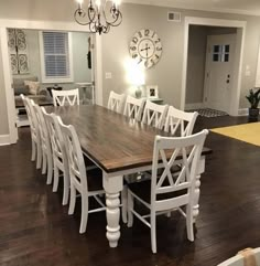 a dining room table with white chairs and a clock on the wall