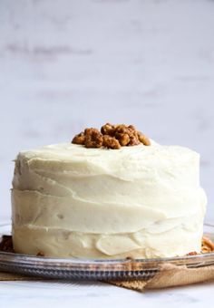 a white frosted cake with walnuts on top sitting on a glass platter