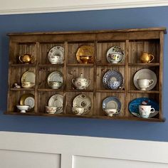 a wooden shelf filled with lots of plates on top of a blue wall next to a white door