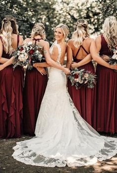 a group of women standing next to each other wearing red dresses and holding bouquets