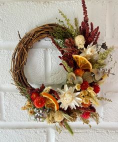 a wreath with dried flowers and oranges hanging on a brick wall in front of a white brick wall