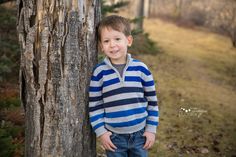 a young boy standing next to a tree