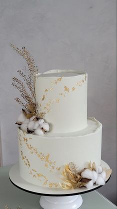 a three tiered white cake with gold leaf decoration on the top and bottom layer