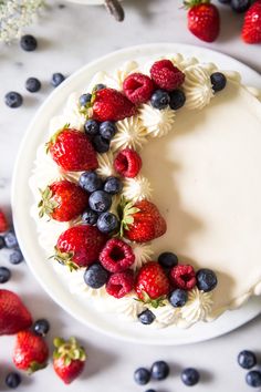 a white cake topped with berries and blueberries on top of a table next to flowers