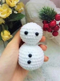 a hand holding a small crocheted snowman ornament next to a potted plant