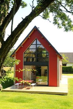 a small red house sitting on top of a lush green field next to a tree