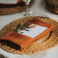 a place setting with orange napkins and an olive branch