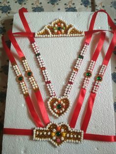 an elaborate necklace and bracelet made from pearls, glass beads and red ribbon on a white card