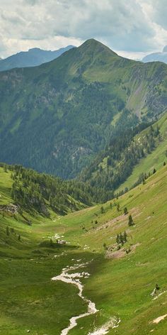 there is a stream running through the grass in this mountain valley with mountains in the background