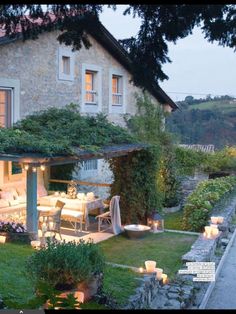 an outdoor dining area with candles lit in front of a house and garden at dusk