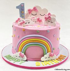 a pink birthday cake decorated with rainbows and clouds