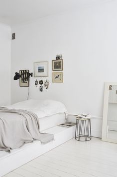 a white bedroom with pictures on the wall and a bed in front of a mirror