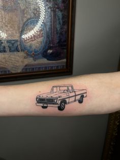 a black and white photo of a truck tattoo on the right arm, with an old car in the background