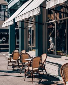 tables and chairs are lined up on the sidewalk outside a coffee shop with white awnings