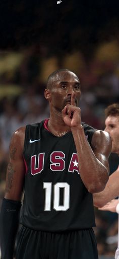 a basketball player holding his hand to his mouth while standing next to another player in front of him