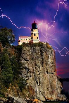 a light house sitting on top of a cliff next to the ocean with lightning in the sky