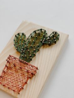 a piece of wood with wire attached to it on top of a white table next to a plant