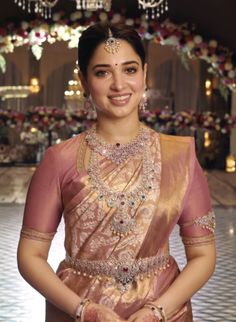 a woman in a pink and gold sari posing for the camera with her hands on her hips