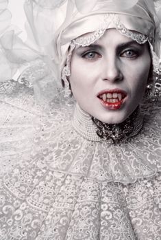 a woman with white makeup and red lips wearing a headdress is posing for the camera