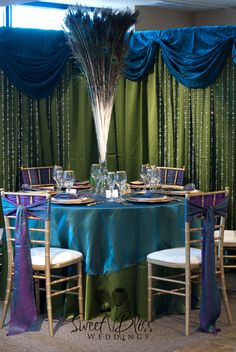 the table is set up for a party with peacock feathers on it and blue drapes