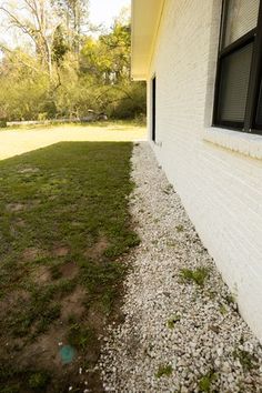 the side of a house with grass and rocks on the ground next to an open window