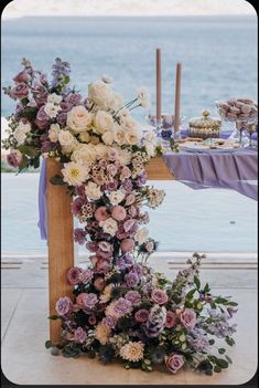 an arrangement of flowers on a table by the water at a wedding reception with purple and white decor