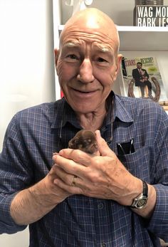 an older man holding a small bird in his hands while standing next to a bookshelf