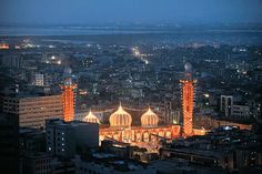 an aerial view of a city at night with tall buildings lit up in orange and white