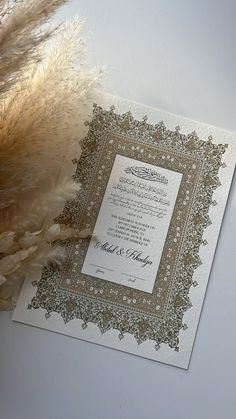 the wedding card is next to some dried flowers and a feathery bouquet on a white surface