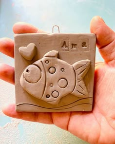 a hand is holding a clay ornament with a fish and heart on it