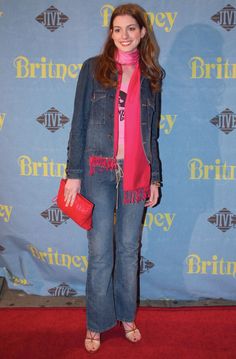 a woman standing in front of a blue backdrop holding a red purse and smiling at the camera