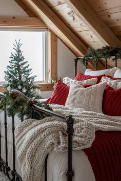 a bed with red and white pillows under a window next to a christmas tree in the corner