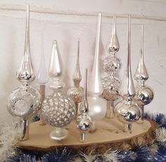 an assortment of silver glass ornaments on a wooden stand with blue tinsel and white feathers