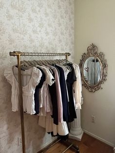 a rack with clothes hanging on it in front of a mirror and wallpapered wall