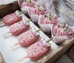 some pink cupcakes with unicorn faces on them in a wooden box next to tulle