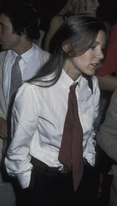 a woman wearing a white shirt and red tie standing in front of a group of people