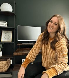 a woman sitting on a couch in front of a tv and bookshelf with shelves behind her