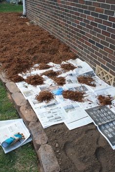 a pile of dirt sitting on top of a newspaper next to a brick wall and grass