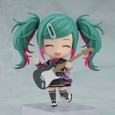 a doll with green hair holding a guitar and wearing a black outfit, standing on a clear base