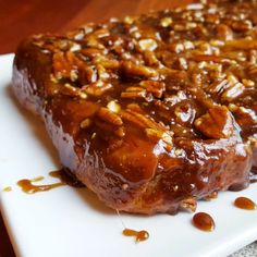 a piece of meat covered in caramel sauce on a white plate with pecans